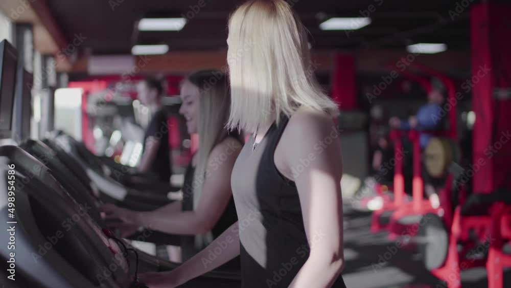 Two fit blonde women uses Treadmill to warm up before training Two fit blonde women uses Treadmill to warm up before training