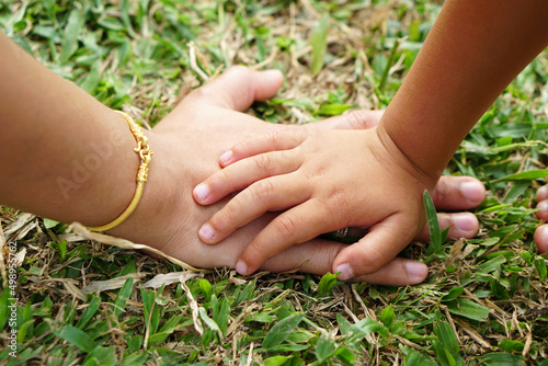 Children's hands and mother's hands touch the grass and the earth.