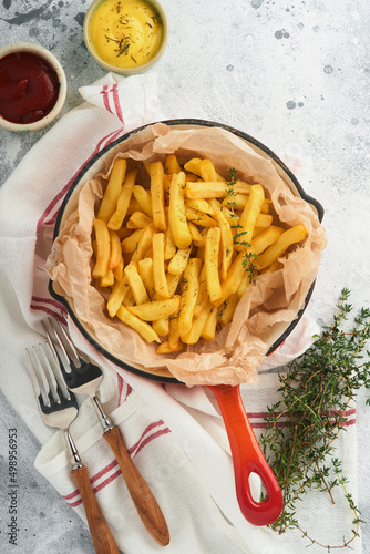 French fries. Tasty French fries server in red cast iron skillet with tomato and cheese sauce on old gray concretetable background. Diverse Keto Dishes. Fast food and unhealthy food concept. photo