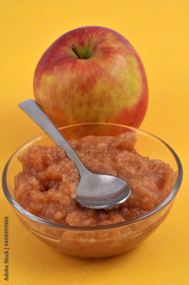 Ramequin de compote avec un pomme au second plan en gros plan sur fond jaune Ramequin de compote avec un pomme au second plan en gros plan sur fond jaune