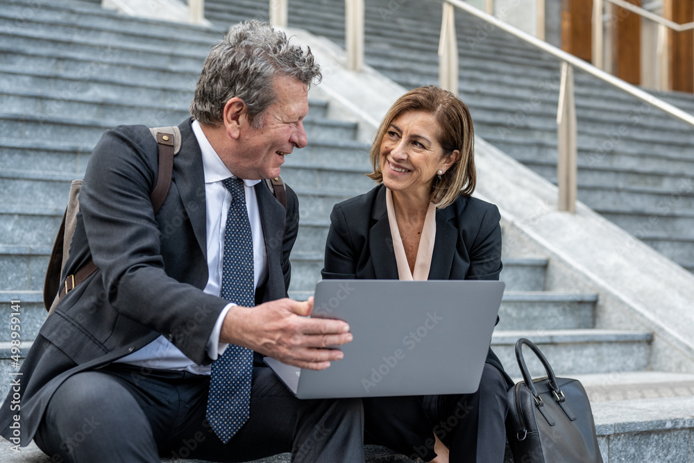 Two business people talking about project strategy outside, businessman discuss project planning with female colleague while having conversation and advice on financial data report on laptop