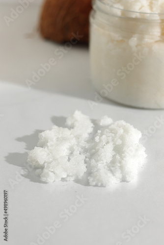 Scattered scrub, jar, coconut on white background. Home spa treatment concept, organic cosmetic. Vertical photo