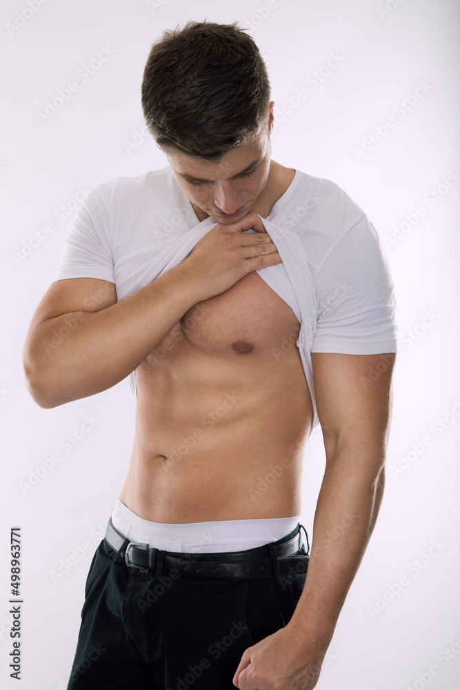 Obraz premium gain muscles and get fit - young man with sixpack pull up his shirt to show his gained abs while look at stomach and being satisfied about visible contours and shape of his upper body