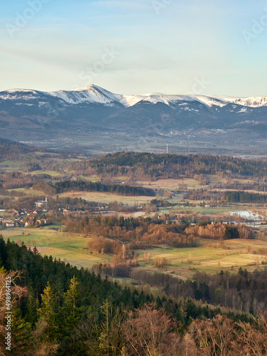 The spring landscape of Rudawy Janowickie at sunrise with the snow-covered Karkonosze Mountains in the background. Vertical view from the top Sokolik Big on forests, fields and mountains.