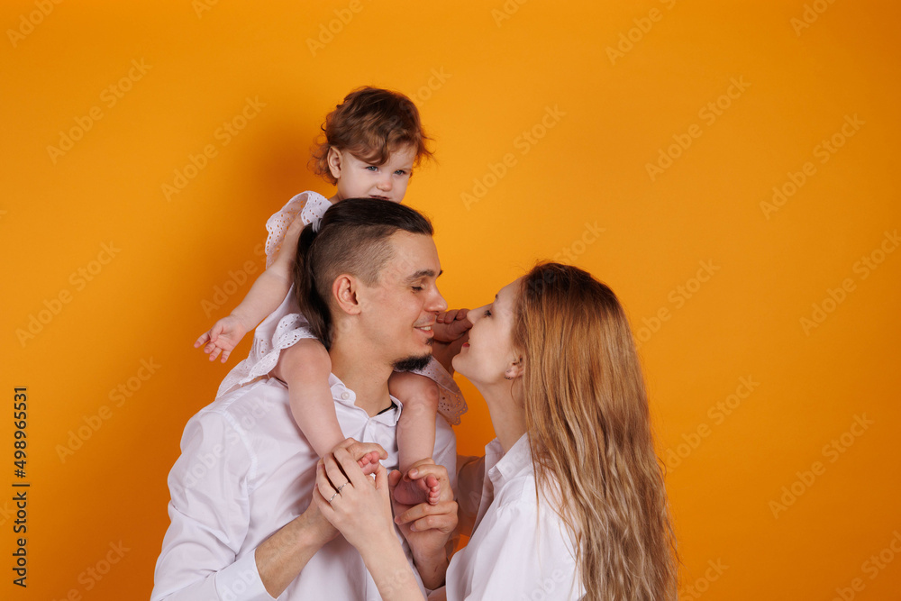Cute family of father, mother and daughter smiling, playing and joking together. Woman and man kisses and embraces. Happy family with a baby girl on hands kissing daughter Cute family of father, mother and daughter smiling, playing and joking together. Woman and man kisses and embraces. Happy family with a baby girl on hands kissing daughter