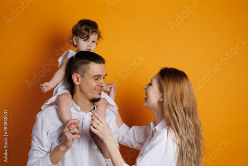 Cute family of father  mother and daughter smiling  playing and joking together. Woman and man kisses and embraces. Happy family with a baby girl on hands kissing daughter