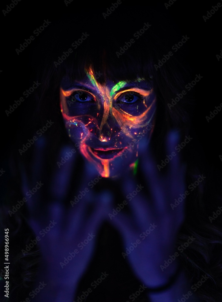 close-up of a woman's face made up with coloured fluorescent paint on her face with her hands close to the camera. close-up of a woman's face made up with coloured fluorescent paint on her face with her hands close to the camera.