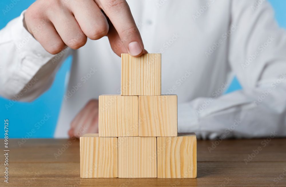Woman building pyramid of cubes on wooden table, closeup. Space for text Woman building pyramid of cubes on wooden table, closeup. Space for text