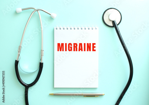 On a blue background, a stethoscope and a white notepad with the words MIGRAINE. photo