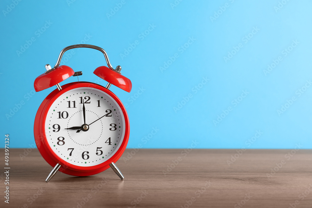 Red alarm clock on wooden table against light blue background, space for text Red alarm clock on wooden table against light blue background, space for text