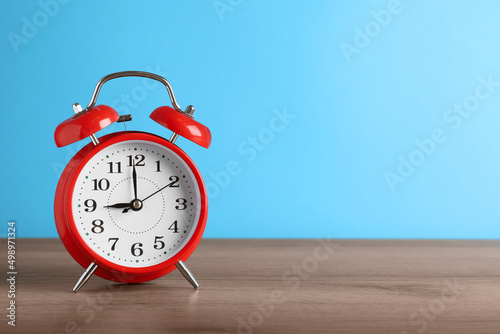 Red alarm clock on wooden table against light blue background, space for text