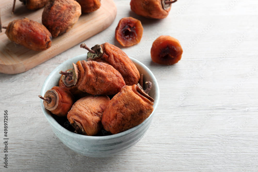 Bowl with tasty dried persimmon fruits on wooden table, space for text Bowl with tasty dried persimmon fruits on wooden table, space for text