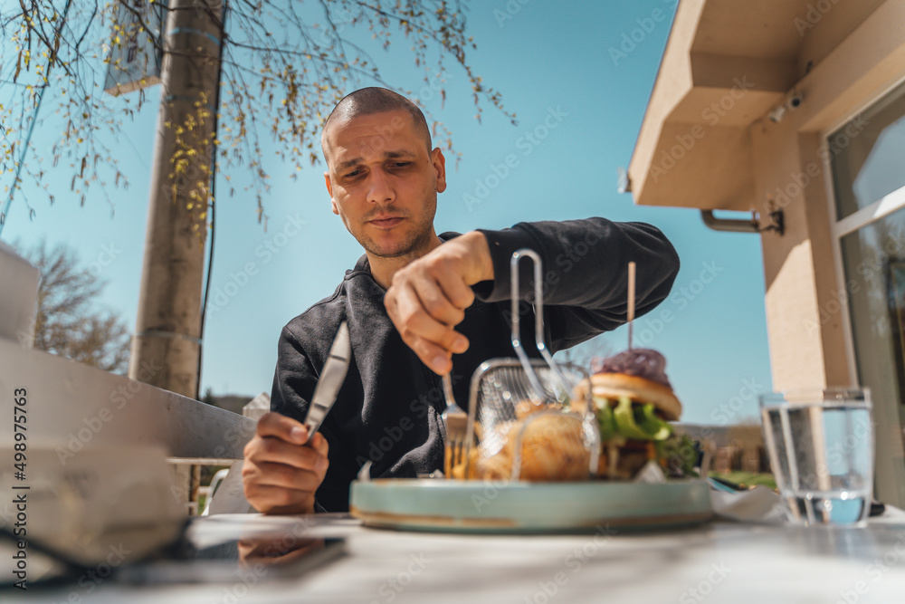 A man is eating burger outside during the day