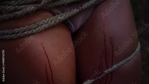 A woman in underwear is tied with a rope to a tree in the woods. Close-up photo
