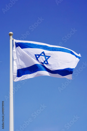 Israel flag waving against clean blue sky, close up. Israel flag in the blue sky. Flag Israel on blue sky background