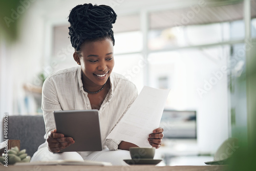 Ive done well with expenses this month. Shot of a businesswoman using her digital tablet while reading paperwork. photo