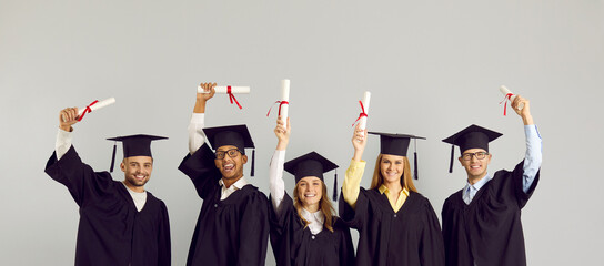 Congrats, grad. Happy proud international multiracial multiethnic college or university students in graduate hats and robes standing on grey studio background and showing diplomas. Graduation concept
