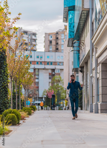 Stylish man wearing blue suit and denim pants walking on urban place