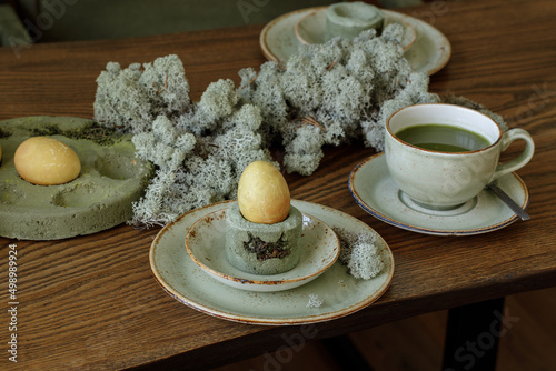 Table setting for Easter dinner decorated with forest moss, eggs coloured with matcha tea in moss green cement tray. photo