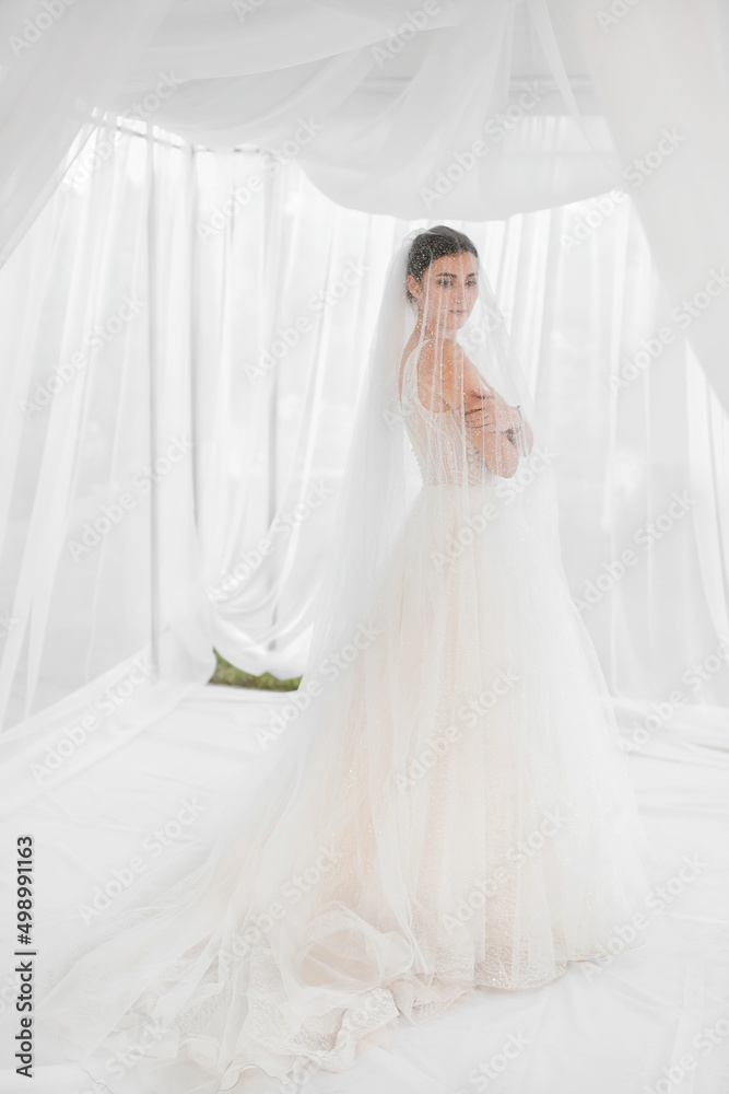 Happy bride with a beautiful long veil and a wedding bouquet. White curtains