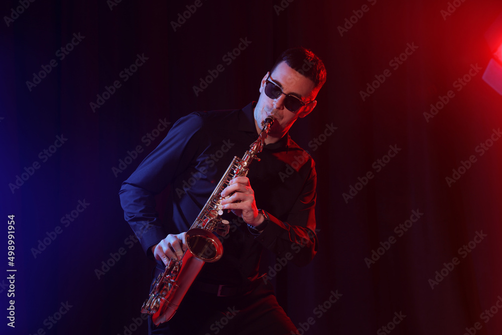 Naklejka premium Young man playing saxophone on dark background