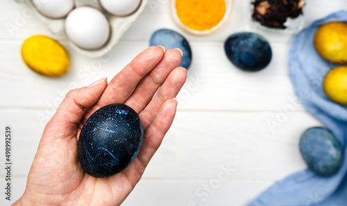 Woman's hand holds Easter egg dyed blue. Coloring eggs for Easter with natural food coloring at home. Top view. Close-up. Selective focus.