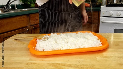 Home cooking - Pouring and spreading vinegar mix with sugar and salt ang kombu preparing rice for sushi.