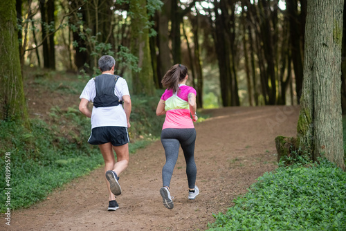 Back view of active man and woman jogging in forest. Two sporty people in sportive clothes exercising outdoors. Sport, hobby concept