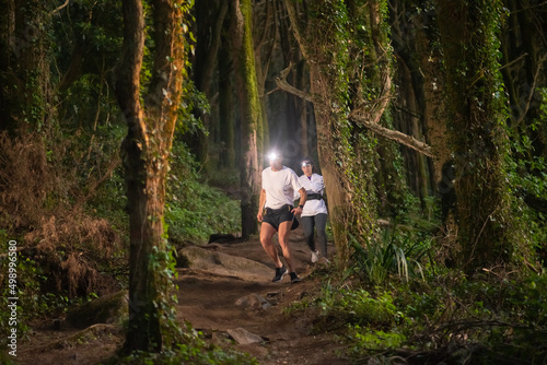 Active man and woman walking in forest at night. Two sporty people in sportive clothes spending time outdoors. Leisure, nature, hobby concept