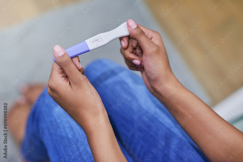 Well, this is a surprise. Shot of an unidentifiable woman holding a pregnancy test while sitting in her bathroom. - obrazy, fototapety, plakaty 