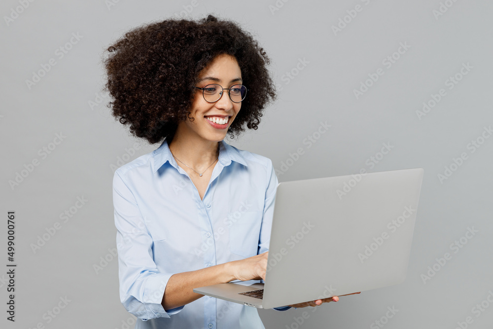 Young happy fun employee business corporate lawyer woman of African American ethnicity in classic formal shirt at office hold use work on laptop pc computer isolated on grey color background studio. Young happy fun employee business corporate lawyer woman of African American ethnicity in classic formal shirt at office hold use work on laptop pc computer isolated on grey color background studio.