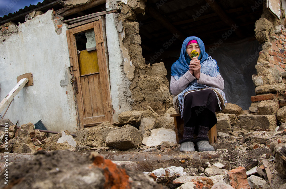 A woman in front of a destroyed house in Ukraine. A woman prays for peace. War in Ukraine. Grandmother in the ruins of the house after the war. Grandmother prays for an end to the war.