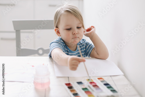 Child painting and drawing with watercolor paint at white table. Development of creative potential in children. 