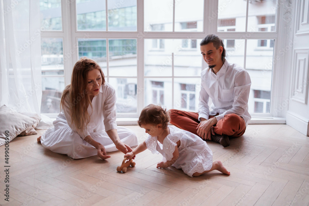 Cute family of father, mother and daughter smiling, playing and joking together. Family playing at window with toy, girl flying Cute family of father, mother and daughter smiling, playing and joking together. Family playing at window with toy, girl flying