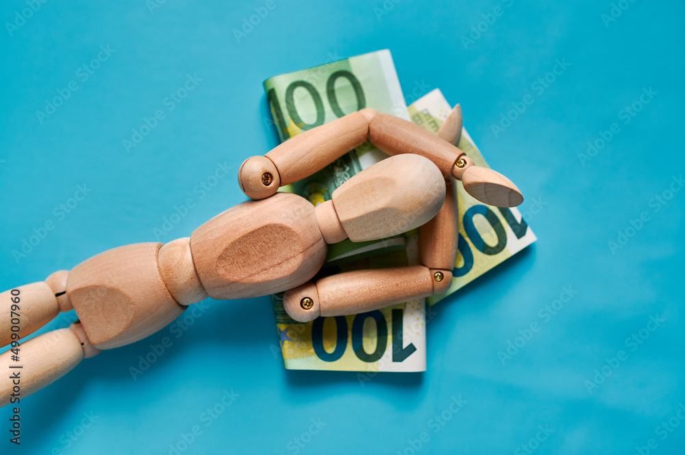 A wooden mannequin rests on 100 euro banknotes. Business concept.