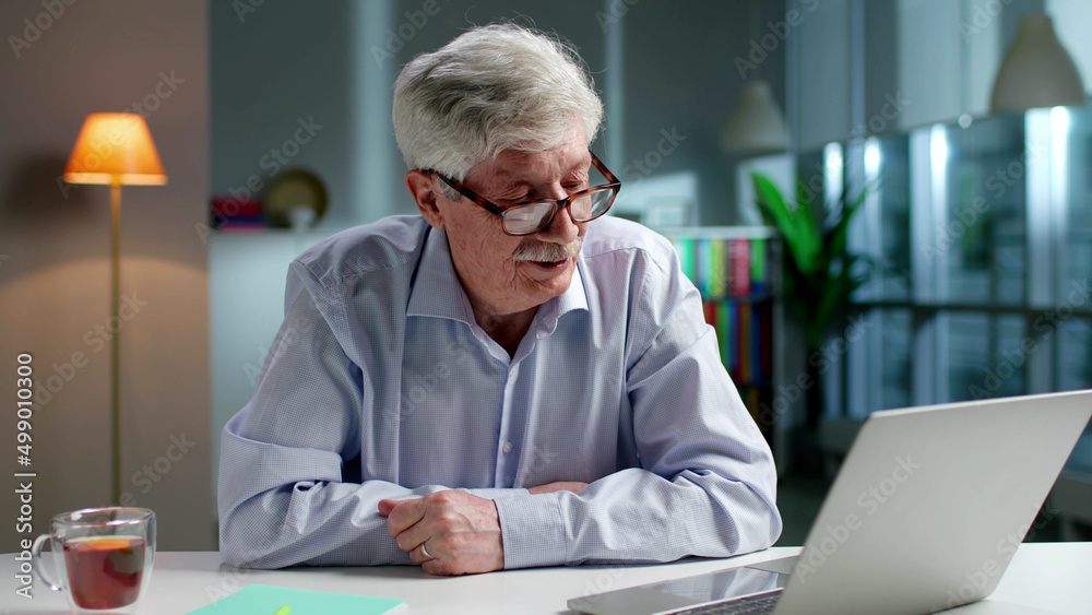 Elderly man having video call on laptop sitting at desk in living room Elderly man having video call on laptop sitting at desk in living room