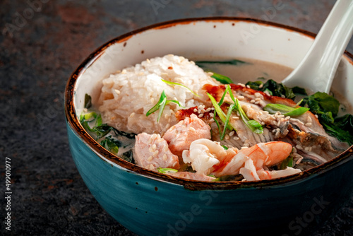 Oriental seafood soup with cream in a blue ceramic bowl. Fish Soup with salmon, eel, shrimp, rice, onion, sesame and seaweed, close up