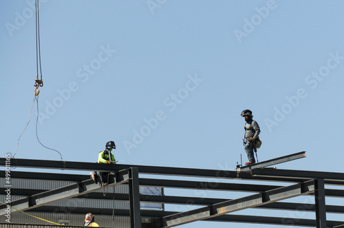 Welders installing steel beams on top of a commercial building under construction against a blue sky