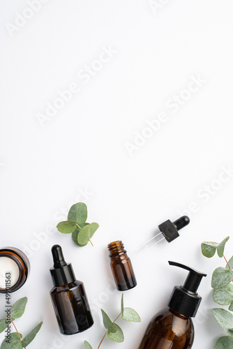 Top view vertical photo of glass bottles cream jar and eucalyptus on isolated white background with copyspace