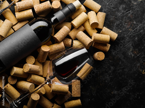 A bottle of red wine and a wine glass with wine lie on wine corks. Isolated on a dark background. There are no people in the photo. There is free space to insert. Restaurant, hotel, bar.