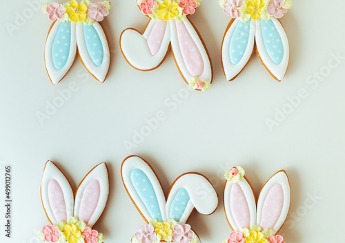 Gingerbread cookies in the shape of cute Easter bunny ears decorated with festive icing and flowers on the white background. Flat lay