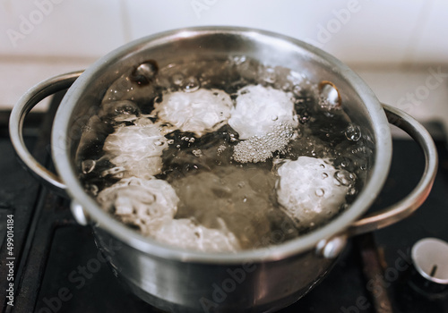Chicken white eggs are boiled in boiling water in a metal pan on the stove.