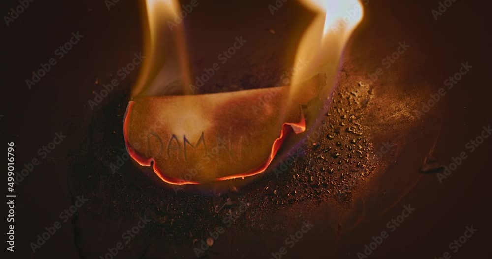 Closeup video of burning paper with DAMNATION written on it