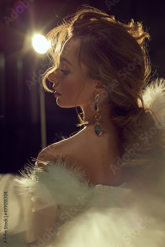 Young attractive women model presenting your jewelry .Wearind white dress with feathers. Nude makeup, perfect skin, long hair. White background.