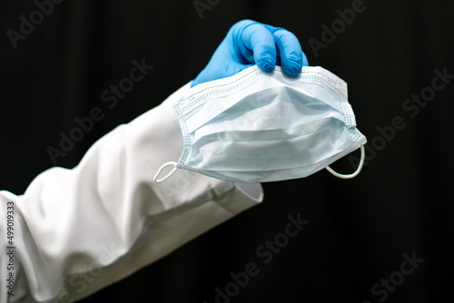 A doctor in a white coat holds a white medical mask in his hand. Gauze bandage as a means of combating coronavirus infection. Treatment and prevention of respiratory infections.