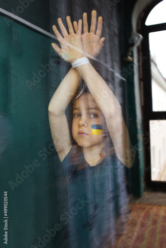 Photography a sad little Ukrainian girl is standing behind the glass with her hands tied up
