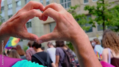 FRANKFURT - July 17, 2021: close-up of male hands in heart form against participants of international LGBT movement, Gay pride parade in city with rainbow flags, mass march of lesbian, gay people photo