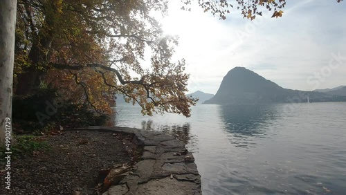 Waterfront of Lugano 's Lake with red and orange autumn trees at sunrise, Switzerland. Popular travel destination