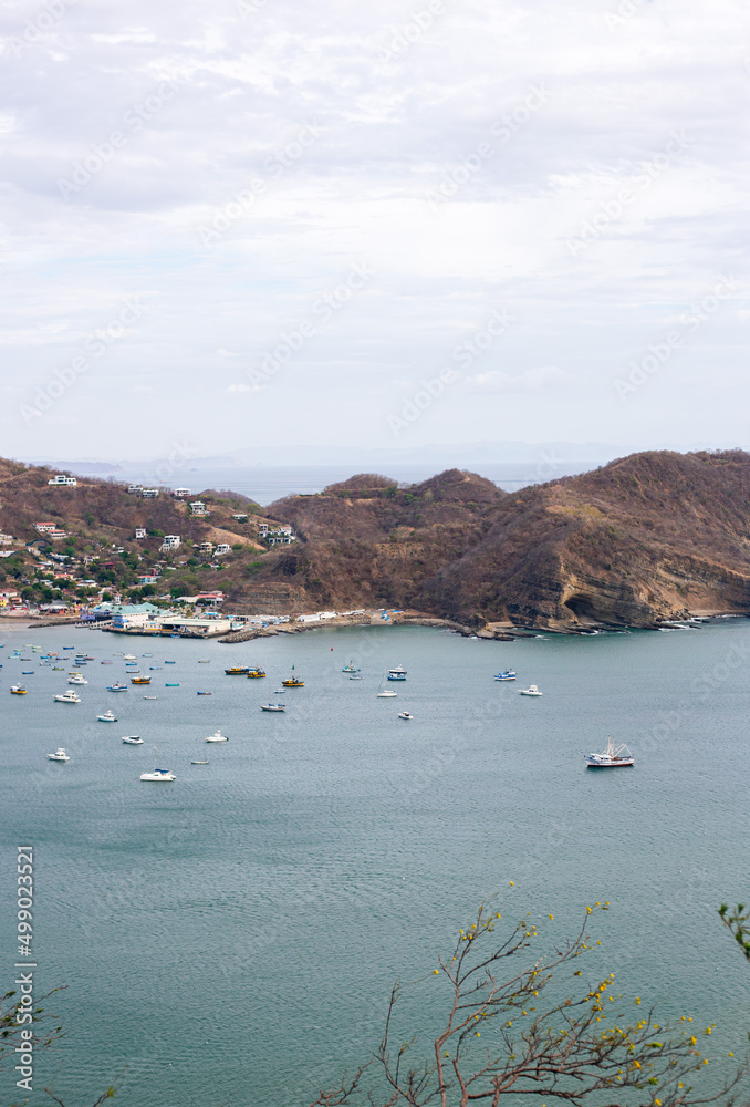 Fototapeta premium vertical format aerial view of a beach full of tourists, beach surrounded by mountains.