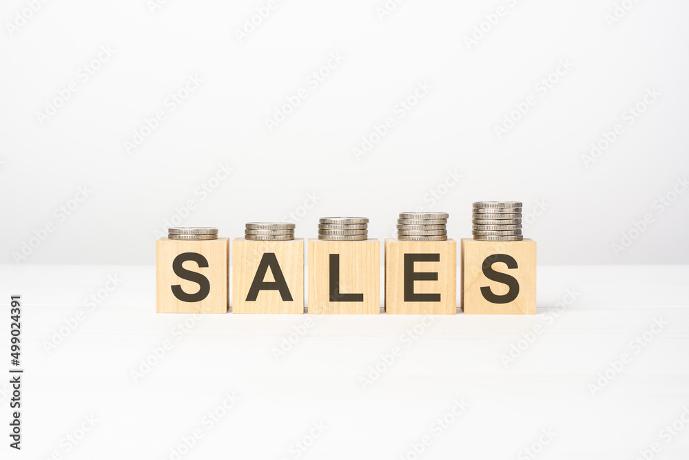 sales text written on wooden block with stacked coins on white background sales text written on wooden block with stacked coins on white background
